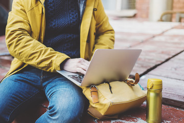 Hipster with yellow backpack, jacket, drink coffee of thermo cup, freelance using computer open...