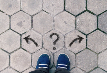 Top view of blue shoes on tiled pavement with questionmark and two arrows, concept of crossroads,...
