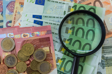 magnifying glass on  Euro banknotes with Euro coins as financial analysis concept