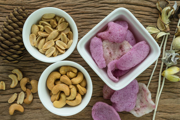 Roasted cashew nuts and peanuts with magenta crisp rice crackers appetizer in white bowl on wooden table