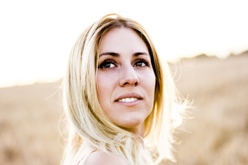 Beautiful blond woman in a red dress, on a wheat field at sunset