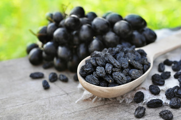 Dried black raisins in wooden spoon with fresh ripe grapes