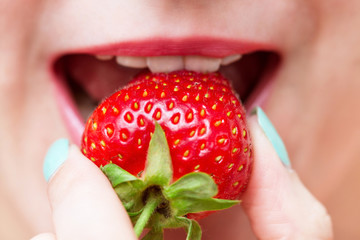Strawberry in a female hand on a background of pink lips. Closeup. Selective focus