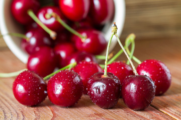 Cherries on wooden table with water drops in the ceramic cup. Closeup. Selective focus