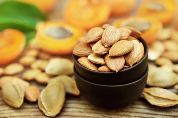Bowl of apricot kernels on pits, stones and fresh apricots background