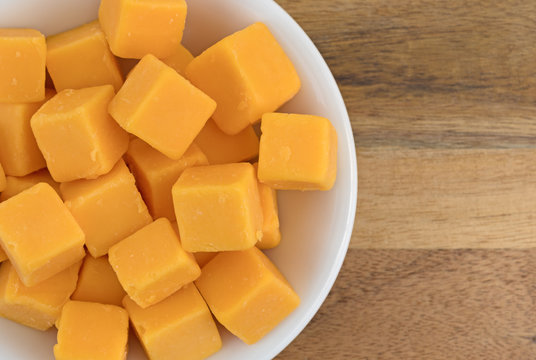 Top close view of cubes of mild cheddar cheese in a white bowl atop a wood counter top.