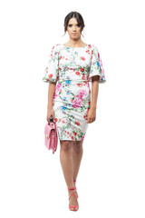 Pretty Latin woman in floral dress with pink bag walking towards camera. Front view. Full body length portrait isolated on white background.