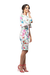 Gorgeous woman in floral dress with bun hairstyle touching hair smiling and looking away. Full body length portrait isolated on white background.