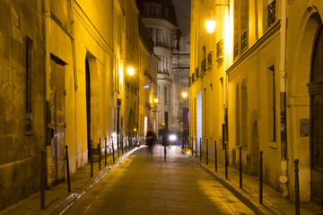 Fototapeta na wymiar Two women walk in blurry motion at night on one of the streets of Le Marais district in Paris. It's night time. The district hosts many outstanding buildings of historic and architectural importance