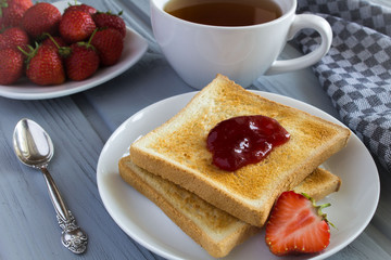 Bread toast with strawberry jam and tea on the grey background