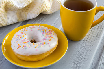Donut on the yellow saucer and tea on the grey background