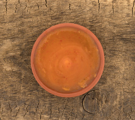 Sweet chili coconut milk sauce in a red clay bowl atop an old wood board.