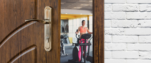 Entrance to gym in fitness club, opened door with woman on elliptical trainer