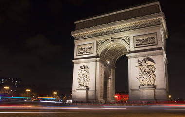Fototapeta na wymiar View of Arc de Triomphe at night. Light trails of cars in motion are also in the view.