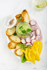 Avocado yogurt dip, sliced fresh vegetables, crisp bread on a plate. Top view