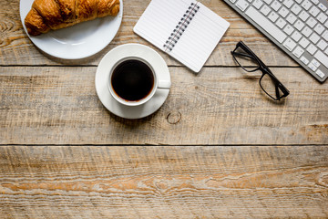 Business breakfast in office with notebook, coffee and croissant on wooden table background top view mockup