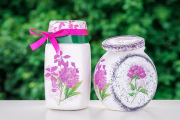 White cans decorated with purple flowers on a natural green background, made by hands, hobby