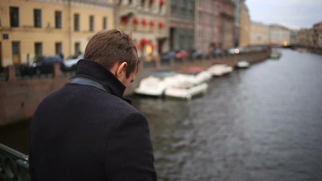 man in a coat stands on a bridge and looks down at the black water. She wants to commit suicide