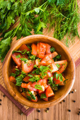 Salad made of tomatoes and fresh herbs in wooden plate. Top view