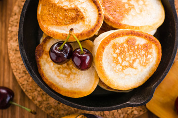 Close-up of fried pancakes in a iron pan and ripe cherries