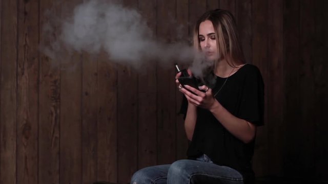 The girl smokes electronic cigarette and use the phone
