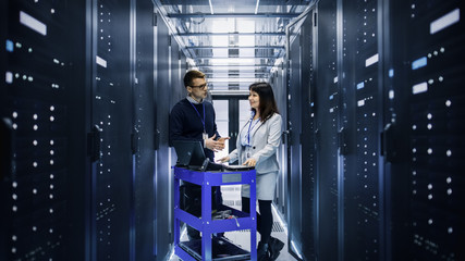 Caucasian Male and Asian Female IT Technicians Working with Computer Crash Cart in Big Data Center full of Rack Servers.