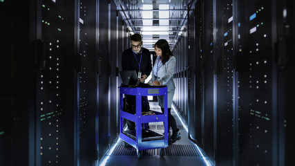 Caucasian Male and Asian Female IT Technicians Working at Large Data Center with Rows of Rack...