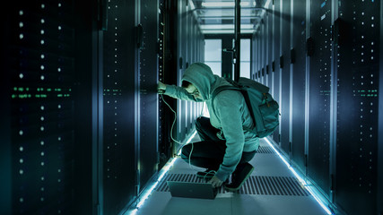 A Hooded Hacker With Laptop Connects to Rack Server and Steals Information from Corporate Data...