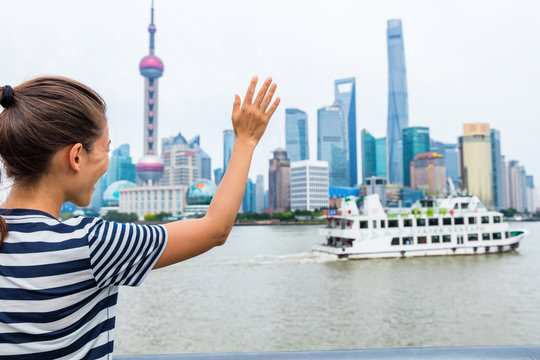 Woman waving goodbye at cruise ship leaving Shanghai city - Travel concept. Asian lady doing hello hand sign at ferry boat cruising on the Bund Huangpu river with Pudong skyline in the background.