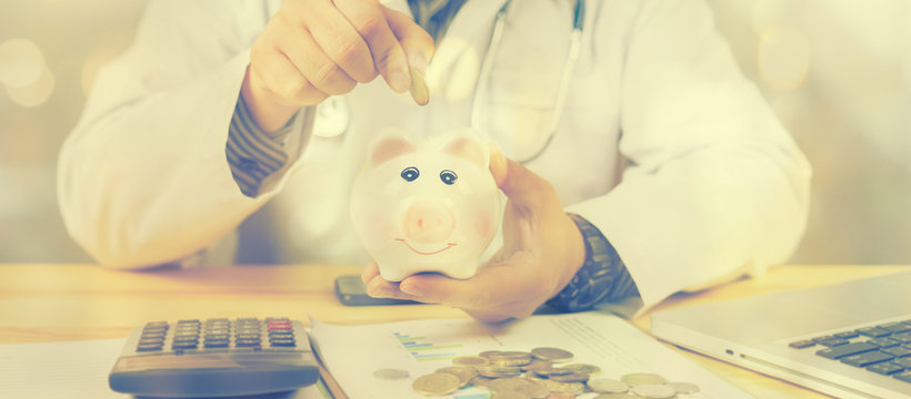 Doctor holding out your piggy bank wanting payment/ Your Savings To Pay Bill, insert coins to it,Stethoscope financial checkup or saving for medical insurance costs money plan fee  Lifestyle concept