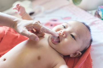 Obraz na płótnie Canvas Asain doctor ,nurse or Mother use finger to clean baby tongue and gum with the clean gauze, first brushing teeth during bathing time.vintage color