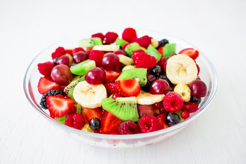 Bowl of tasty fresh fruit salad on white wooden background. Top view.