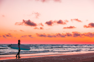Fototapeta na wymiar Girl with surfboard on beach at sunset or sunrise. Surfer and ocean