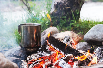 The boiling liquid in a stainless mug stands on the stones in the fire