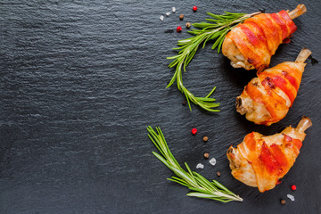Bacon wrapped chicken drumsticks in a black cast-iron skillet on the stone background. - 160963974
