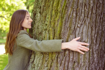 Smiling brunette woman hugging tree trunk