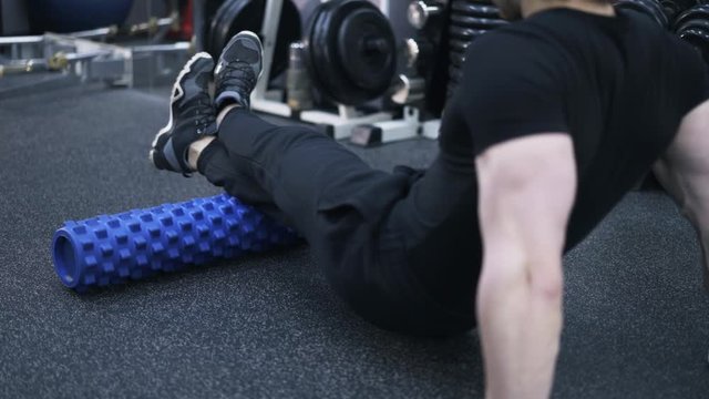 Rear view of young man in black sportswear doing an exercise on a fitness roll in a gym. Concept of staying healthy. Locked down real time close up shot