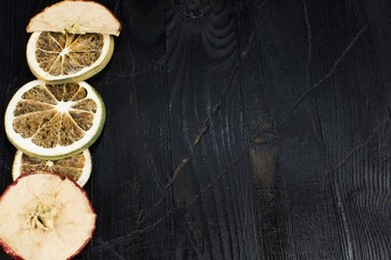 Slices of dried Apple and an orange lying on a black wood texture