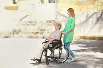 Disabled elderly woman and young caregiver outdoors on sunny day