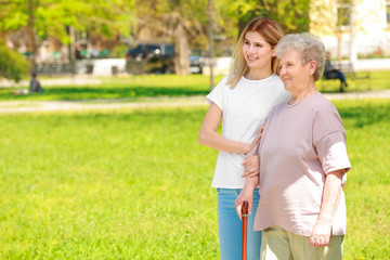 Elderly woman and young caregiver in park on sunny day