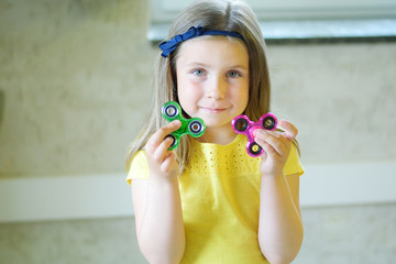 Little beautiful girl in yellow t-shirt is playing with two spinners in hands
