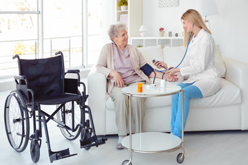 Obraz premium Young nurse measuring blood pressure of disabled elderly woman at home