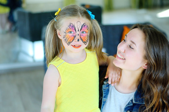 Pretty Girl With Face Painting Of A Butterfly With Babysitter