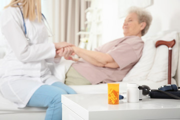Obraz premium Night stand with medicines and blurred nurse examining elderly woman on background