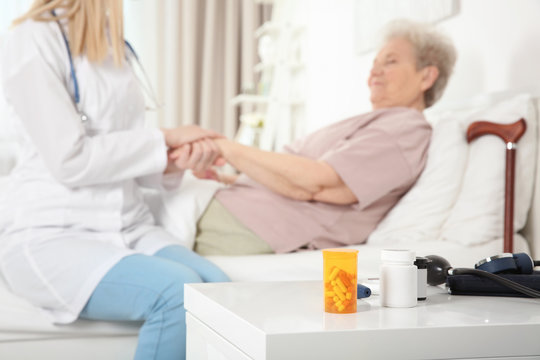Night stand with medicines and blurred nurse examining elderly woman on background