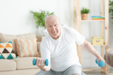 Fototapeta na wymiar Fat senior man training with dumbbells at home. Weight loss concept