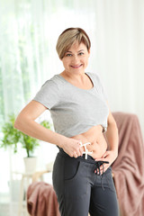 Mature woman with measuring caliper at home. Weight loss concept