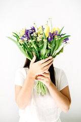 Pretty woman with beautiful flowers bouquet: tulip, chamomile, iris flower at white wall. Floral lifestyle composition.
