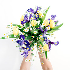 Girl's hands holding beautiful flowers bouquet: tulips, chamomiles, iris flower on white background. Flat lay, top view. Floral composition