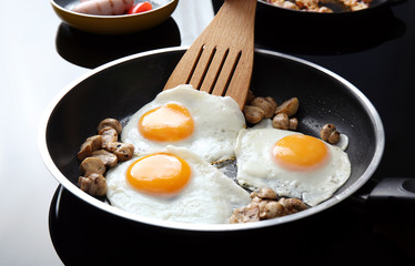 Frying pan with tasty eggs and mushrooms on electric stove